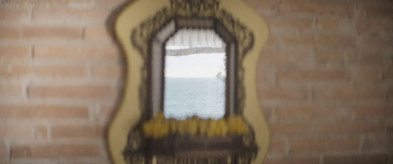 Daaaaaalí! (2023) movie still: A contemplative shot featuring an ornate mirror hung on a textured brick wall, acting as a portal to the sea. The…