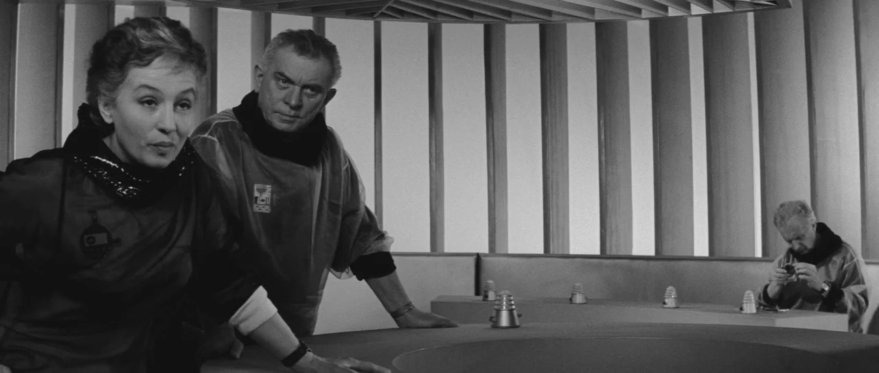 Ikarie XB 1 (1963) movie still: medium — A sterile control center features a circular table and slatted wall partitions. Three people in futuristic…