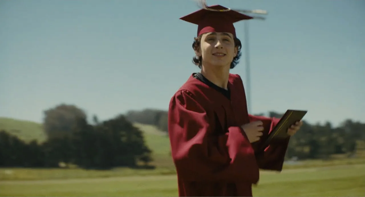 Beautiful Boy (2011) movie still: medium — A grassy athletic field with distant green hills under a bright clear sky. A young man wearing a maroon…