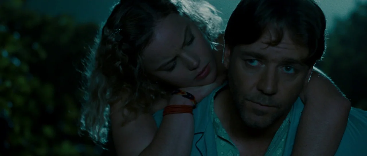 A Good Year (2006) movie still: closeup — A dark outdoor space with dense, out-of-focus foliage creates a backdrop for the pair. A woman with blonde…