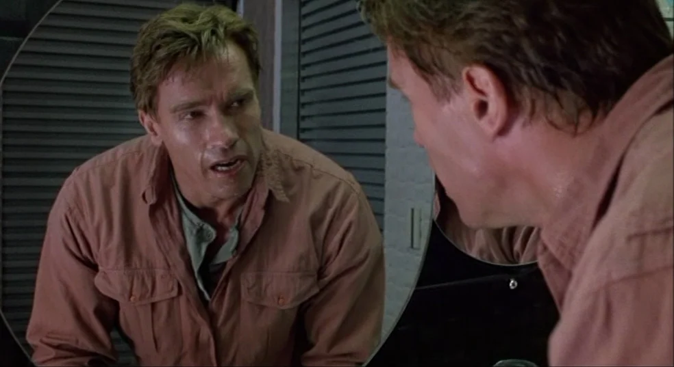 Total Recall (1990) movie still: medium — A man stands in front of a mirror in a dimly lit bathroom. He stares at his own reflection while leaning…