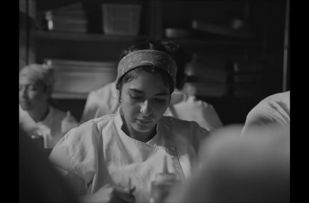 The Kitchen (2012) movie still: medium — A bustling professional kitchen with multiple staff members in white uniforms working near shelves. A young…