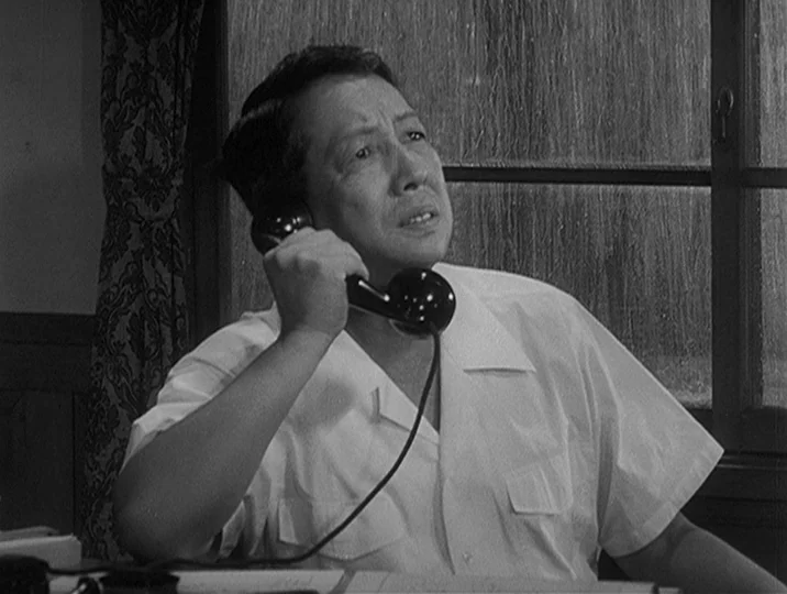 I Live In Fear (1955) movie still: medium — An interior space with a paneled window featuring rain streaks on the glass. A man in a white shirt sits…