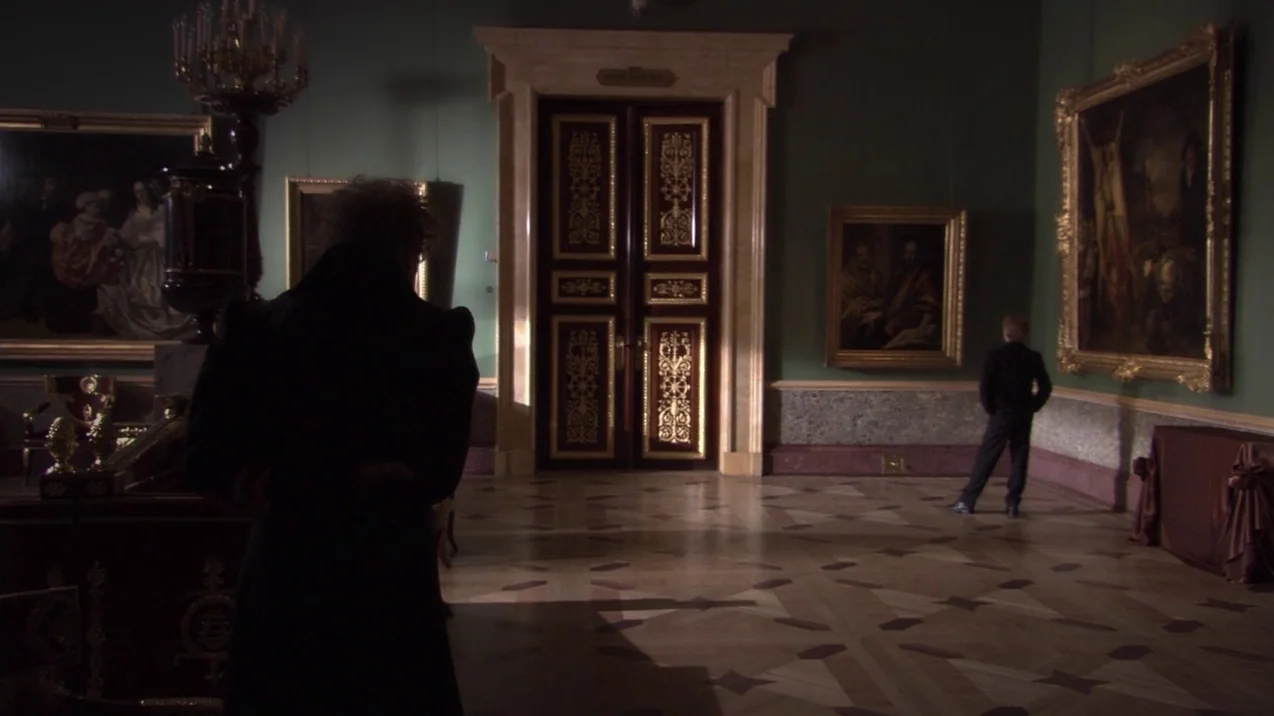 Russian Ark (2002) movie still: wide — A high-ceilinged museum hall features dark green walls decorated with large framed oil paintings. Two men…
