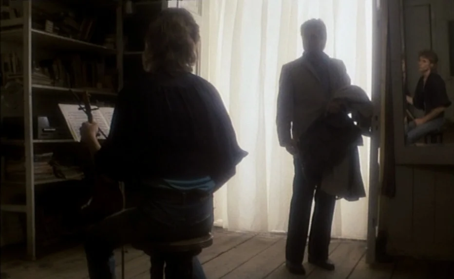 The Fourth Man (1983) movie still: medium — A wooden studio features shelves packed with books and a floor-to-ceiling white curtain doorway. A woman…