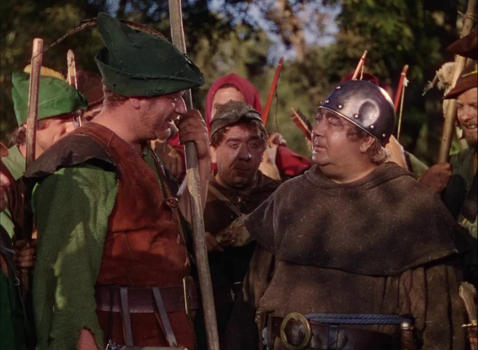 The Adventures of Robin Hood (1938) movie still: medium — A group of medieval archers gathers outdoors within a dense, sun-dappled foliage…