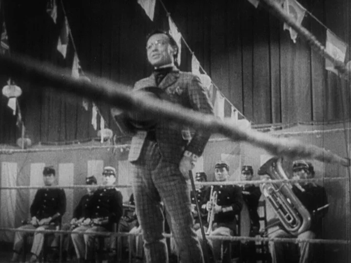 Sanshiro Sugata Part II (1945) movie still: fullbody — A man stands inside a boxing ring decorated with strings of pennants above. Several uniformed…