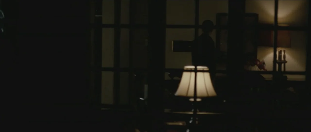 Contraband (2012) movie still: medium — A dimly lit room is partially divided by a dark, paneled wall partition. A person stands in the shadows with…