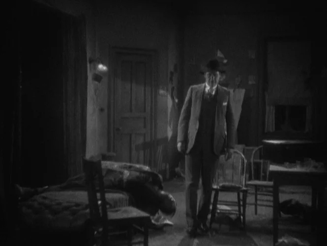 Underworld (1927) movie still: fullbody — A dimly lit, cramped apartment contains a bed with a figure lying prone. A man in a suit and hat stands…