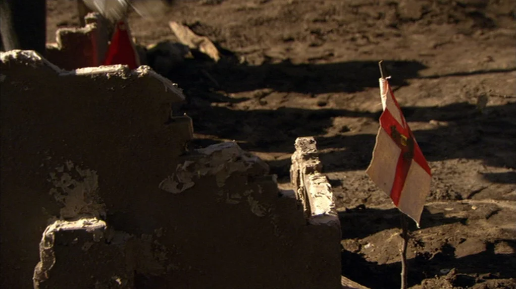 A Cock and Bull Story (2005) movie still: medium — A patch of dry, cracked dirt is littered with low-profile concrete debris and dust. Several small…