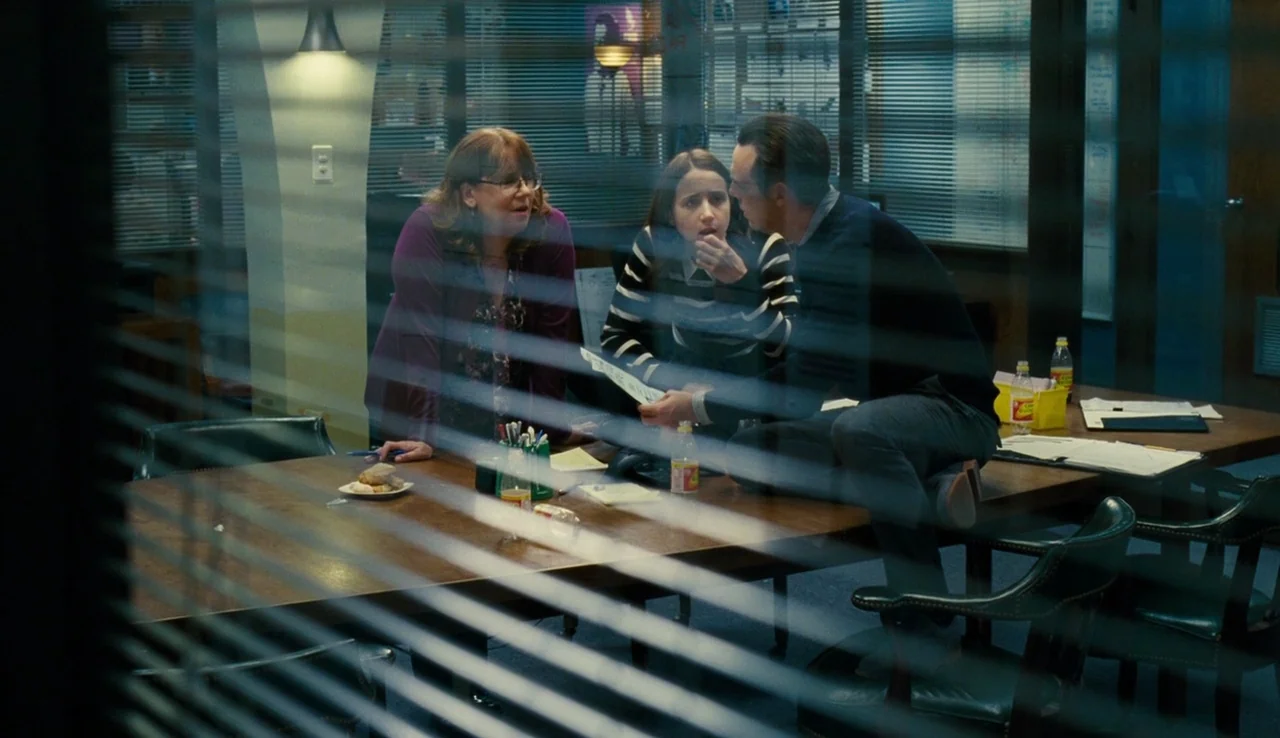 Our Brand is Crisis (2015) movie still: medium — A window-filtered view into a professional workplace room with a large wooden table. Three…