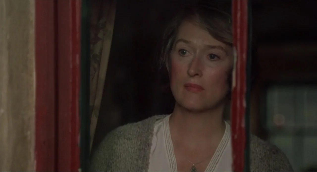 Dancing at Lughnasa (1998) movie still: closeup — A dimly lit interior space with a door slightly ajar revealing a woman. The woman stands behind…