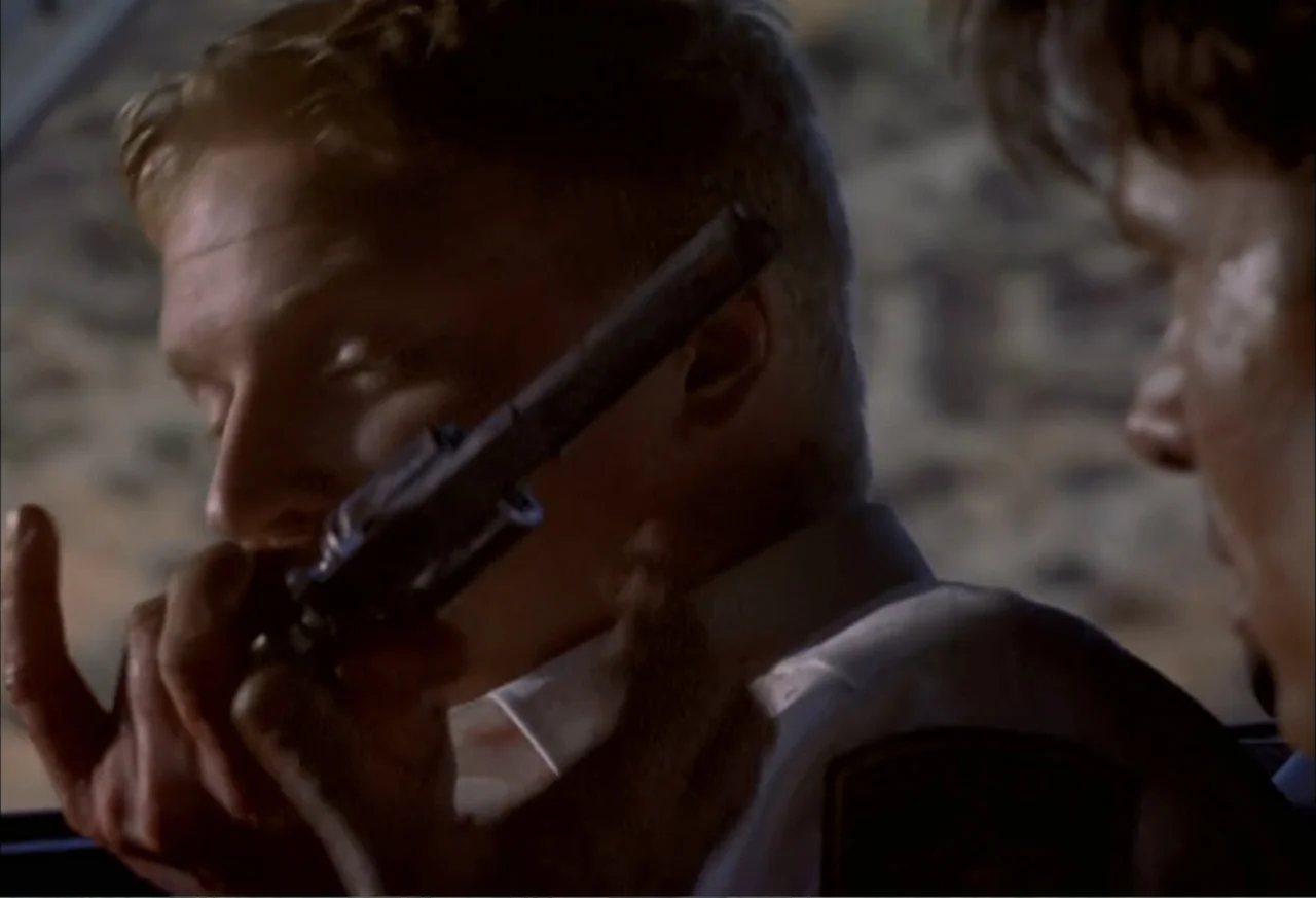 Black Cat Run (1998) movie still: closeup — Inside a vehicle at night, a man holds a handgun against his face. Another person in the foreground…