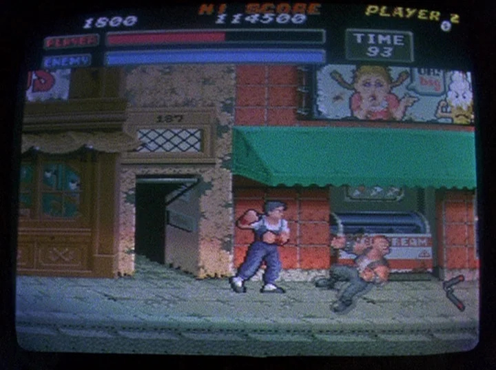 Slacker (1991) movie still: wide — A 16-bit pixel art side-scrolling video game set on a textured city sidewalk. One character punches another in…