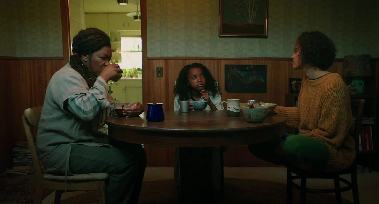 Fast Color (2018) movie still: medium — A wood-paneled room features a round table where three people are eating bowls of food. A framed landscape…