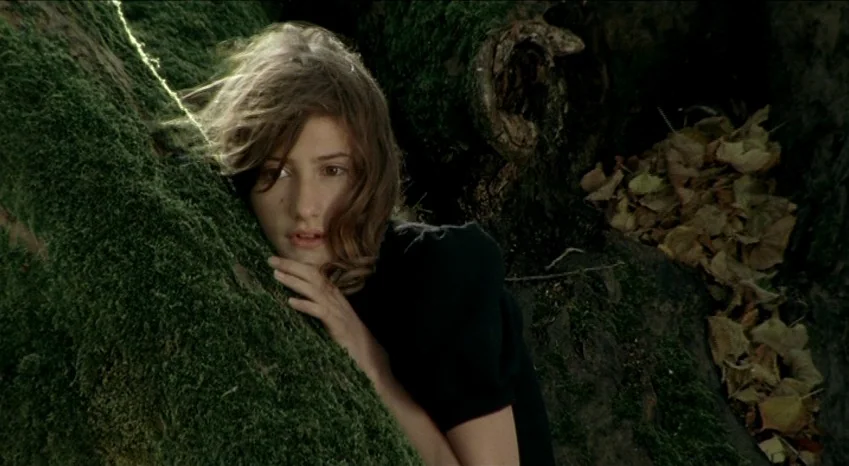 Bluebeard (2009) movie still: closeup — A girl presses her face against the thick moss-covered trunk of a tree. Dry fallen leaves cluster in the…