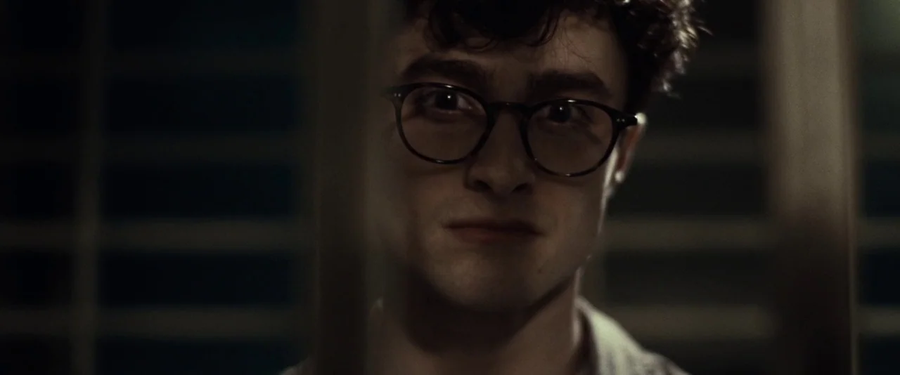 Kill Your Darlings (2013) movie still: closeup — A dimly lit interior space features vertical slats obscuring part of the foreground. A young man…