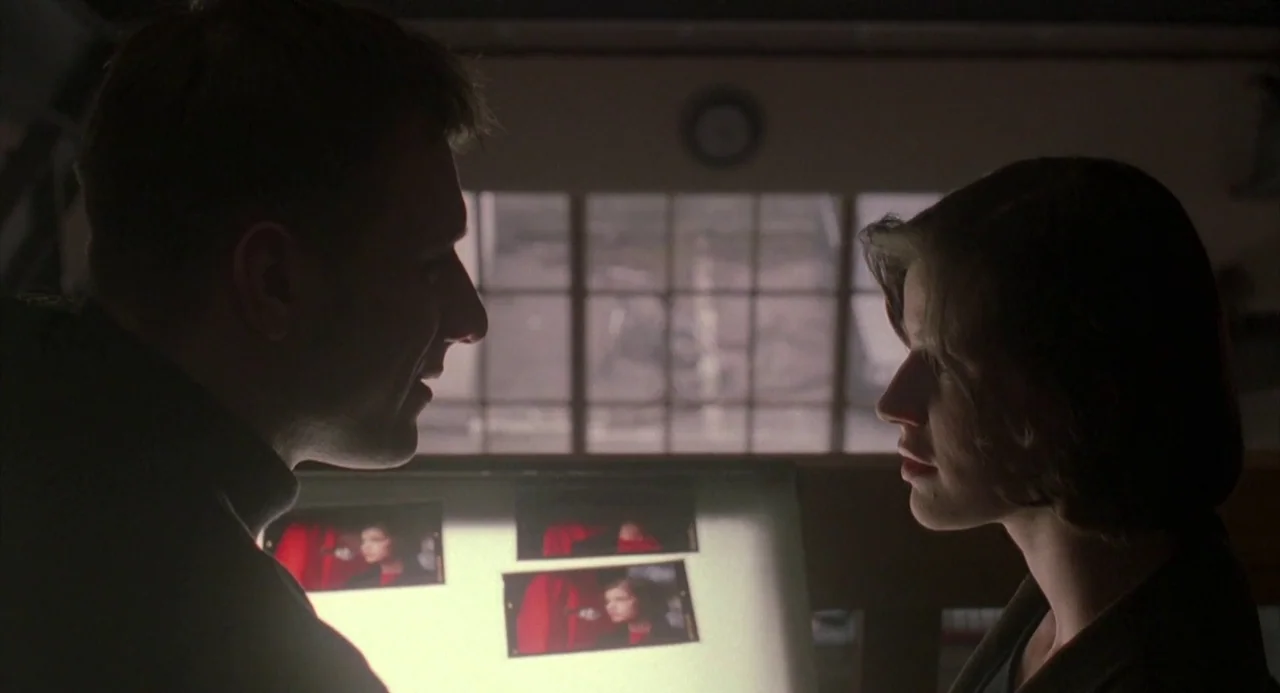 Three Colours: Red (1994) movie still: medium — A dim workspace features a glowing light box illuminating two people in profiles. The subjects stand…