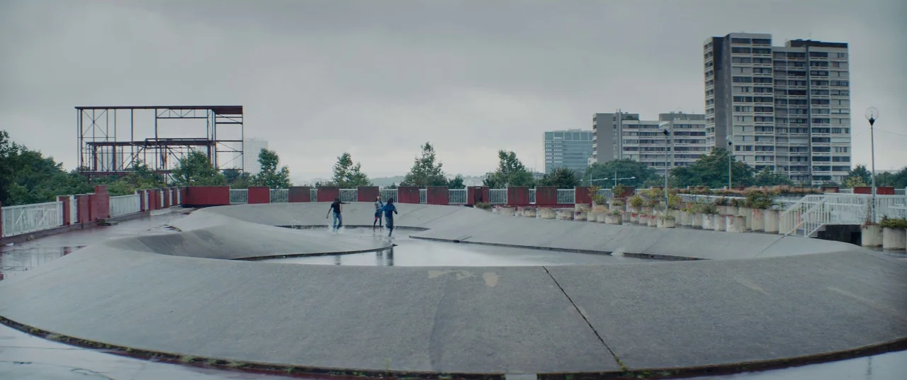 Girlhood (2014) movie still: wide — A concrete rooftop terrace features a circular shallow water basin and surrounding railings. Three figures run…