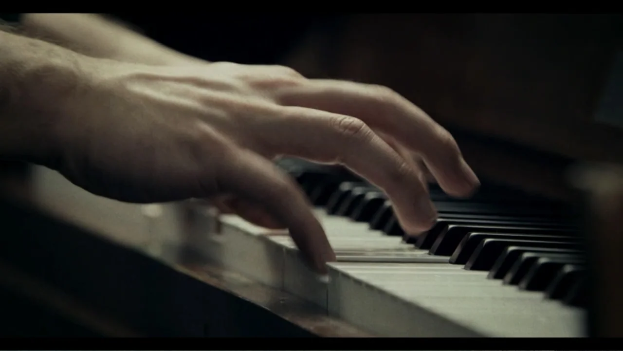 Six by Sondheim (2013) movie still: closeup — A close view of human hands playing a set of wooden piano keys. The instrument is dark and worn,…