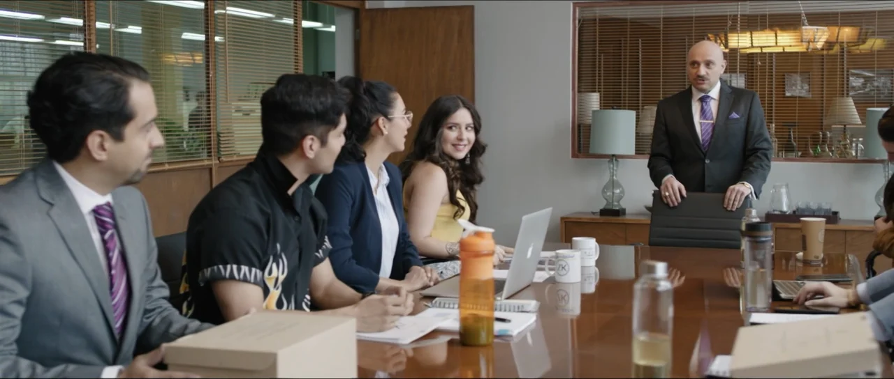 Mirreyes vs Godínez (2019) movie still: medium — A professional conference room with a polished wood table and wooden window blinds. A group of…