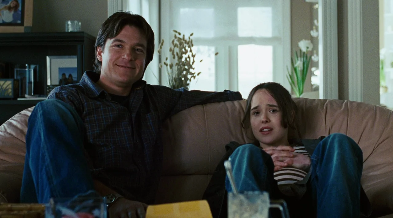 Juno (2007) movie still: medium — A bright domestic interior with a large window and framed photographs on the shelves. A man and a woman are seated…