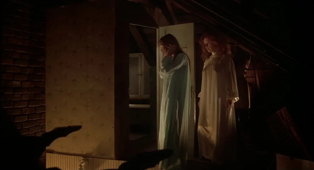 Carrie (1976) movie still: fullbody — An attic space featuring brick walls and low sloping rafters is dimly illuminated. Two women wearing long…