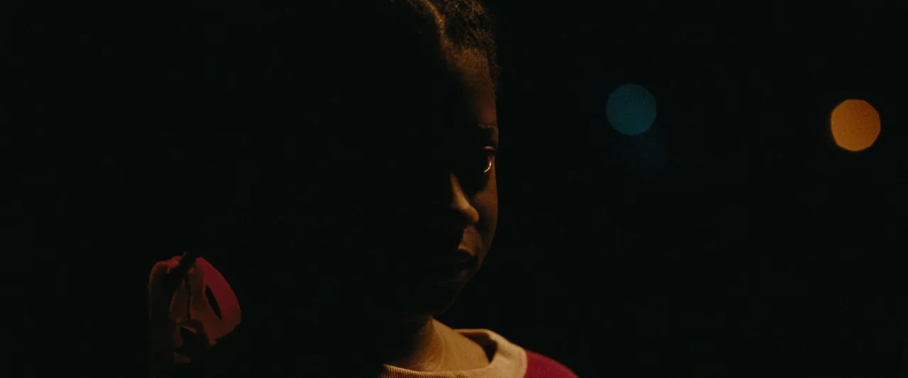 All Dirt Roads Taste of Salt (2023) movie still: closeup — A dark outdoor space at night shows the profile of a young child's face. The subject is…