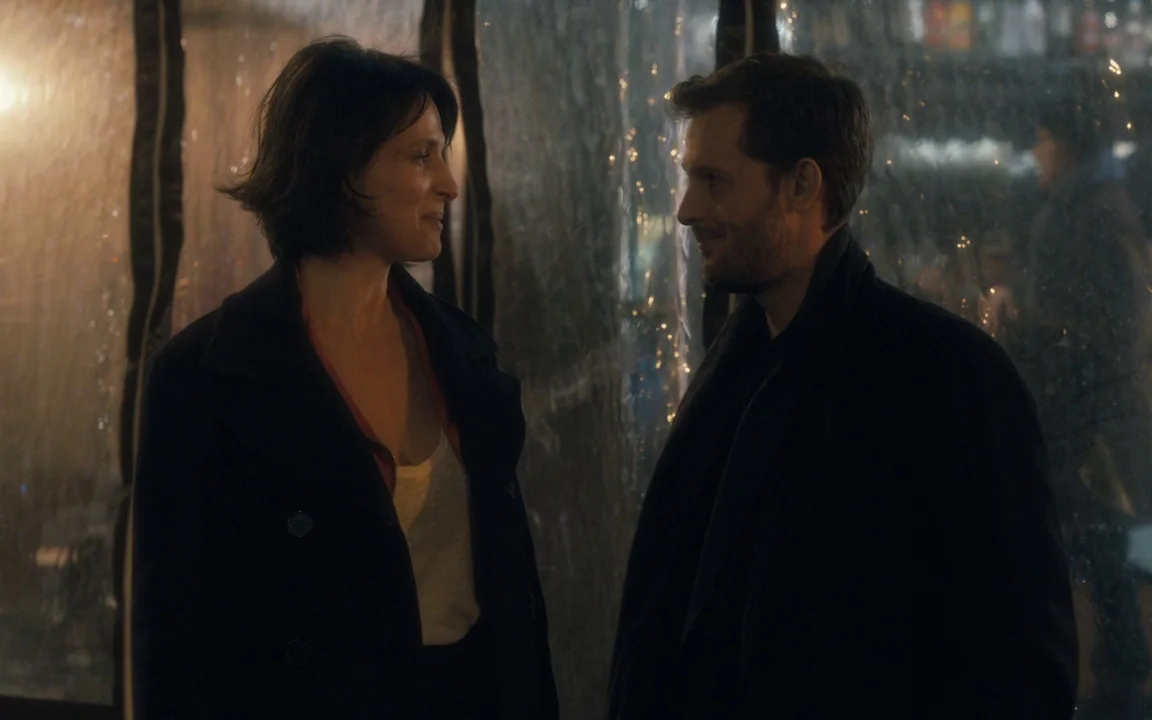 Let The Sunshine In (2017) movie still: medium — Two individuals stand inside a clear plastic enclosure on a dark city street. The man and woman…