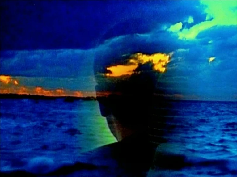 Eloge de L’amour (2001) movie still: medium — A silhouette of a person appears overlaid against a vibrant sea at twilight. The intense color…
