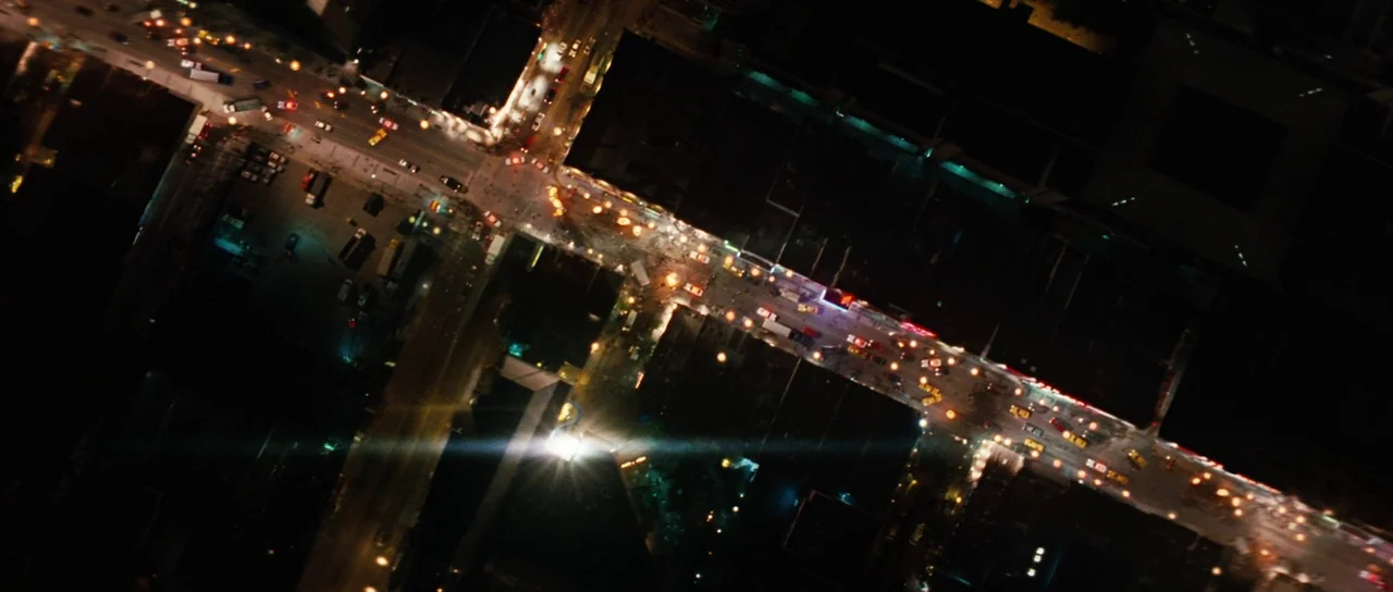 The Incredible Hulk (2008) movie still: establishing — An aerial view captures an urban intersection at night with glowing car headlights. The…