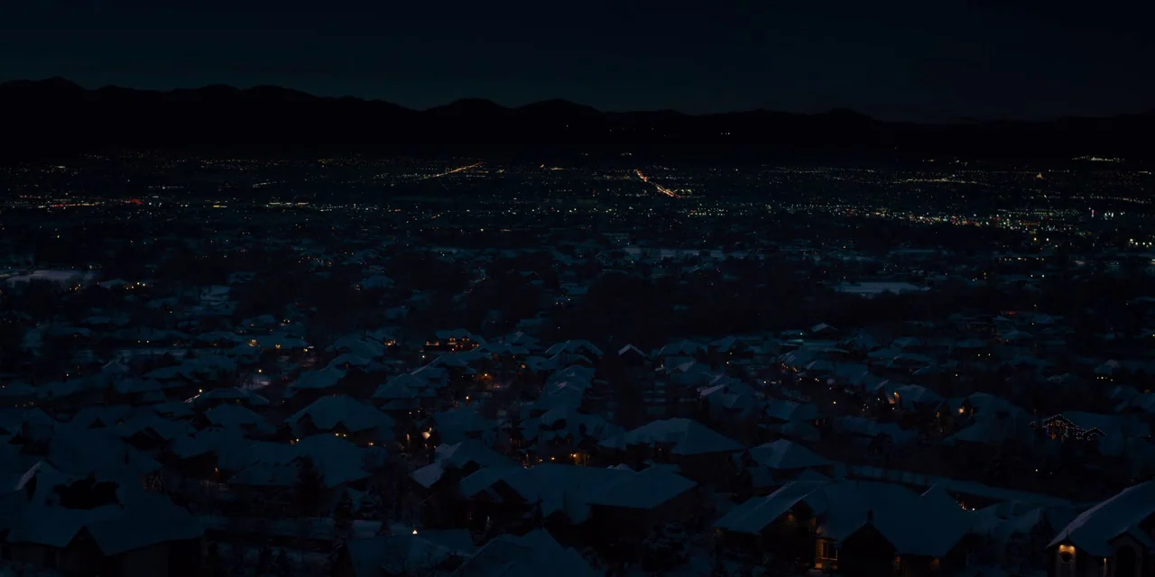 Midsommar (2019) movie still: establishing — An elevated view of a suburban neighborhood at night blanketed in fresh snow. Scattered house lights…
