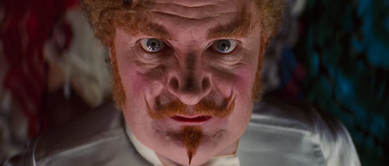 Moulin Rouge! (2001) movie still: closeup — An intense, close-up view of a man with stylized facial hair on a stage. The subject leans forward…