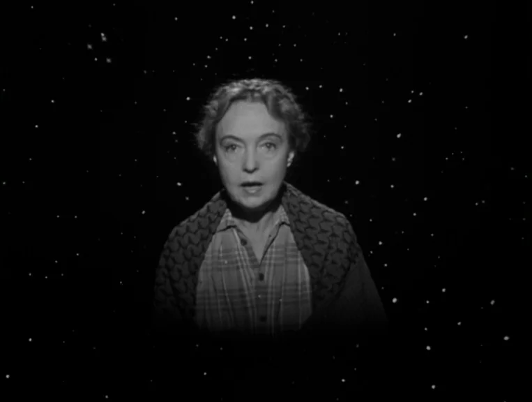 The Night Of The Hunter (1955) movie still: medium — An older woman stands against a black background filled with floating white specks. She stares…