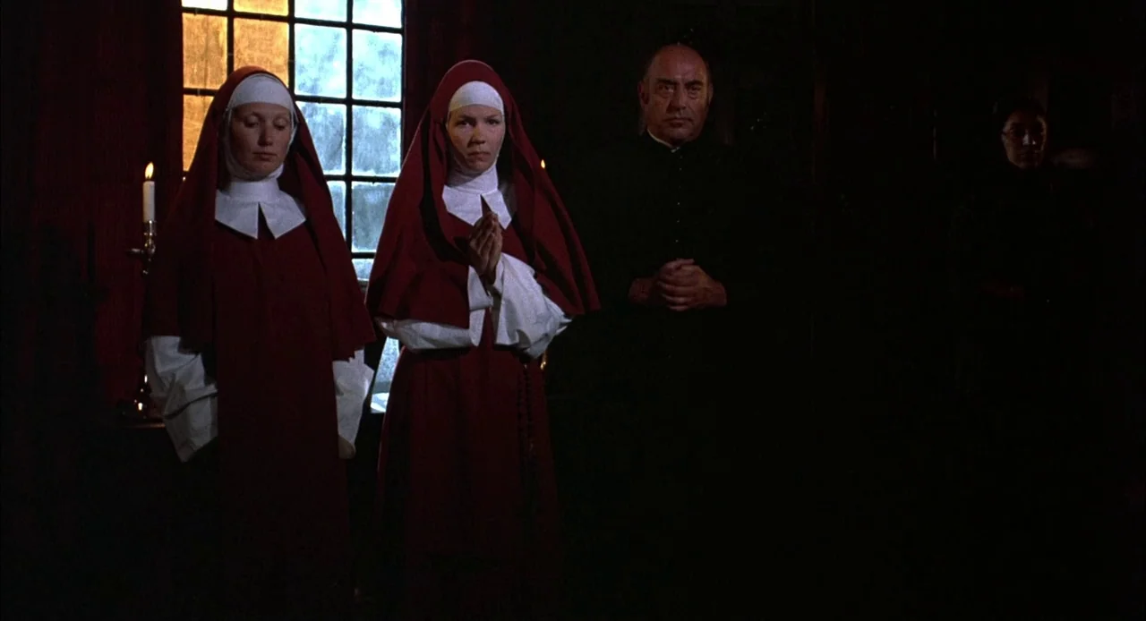 Bring Me The Head of Alfredo Garcia (1974) movie still: medium — A dimly lit room with a paneled window and a single lit candle on a stand. Two nuns…
