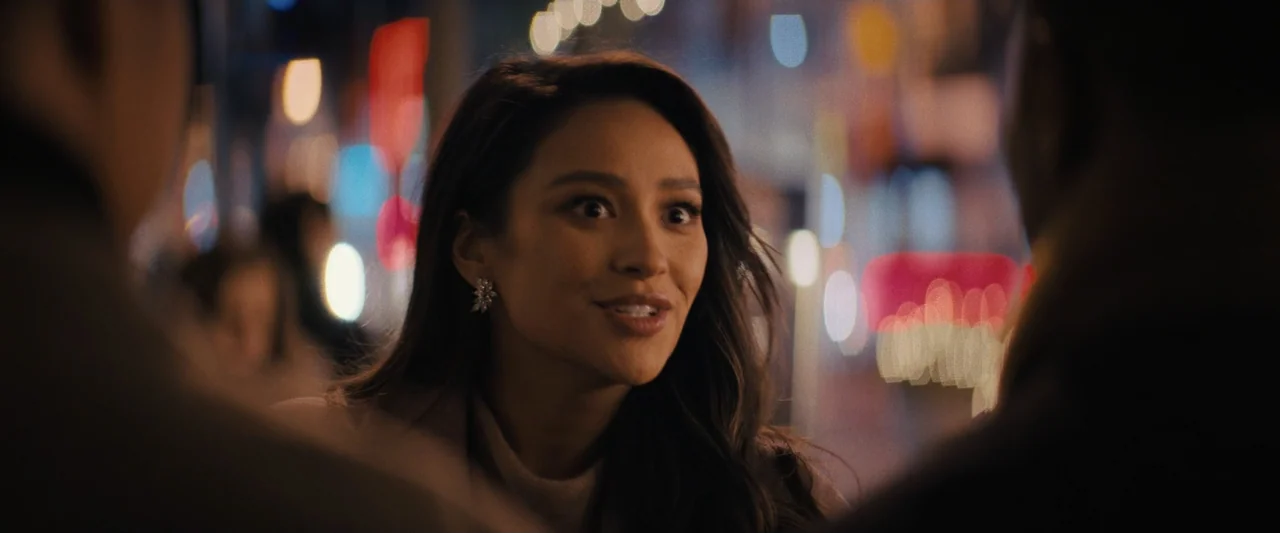 Something from Tiffany's (2022) movie still: medium — A city street at night features heavy bokeh from distant neon and street lights. A woman in a…