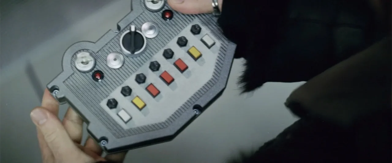 xXx (2002) movie still: closeup — An interior space features a person holding a detailed plastic control interface. The device contains multiple red…