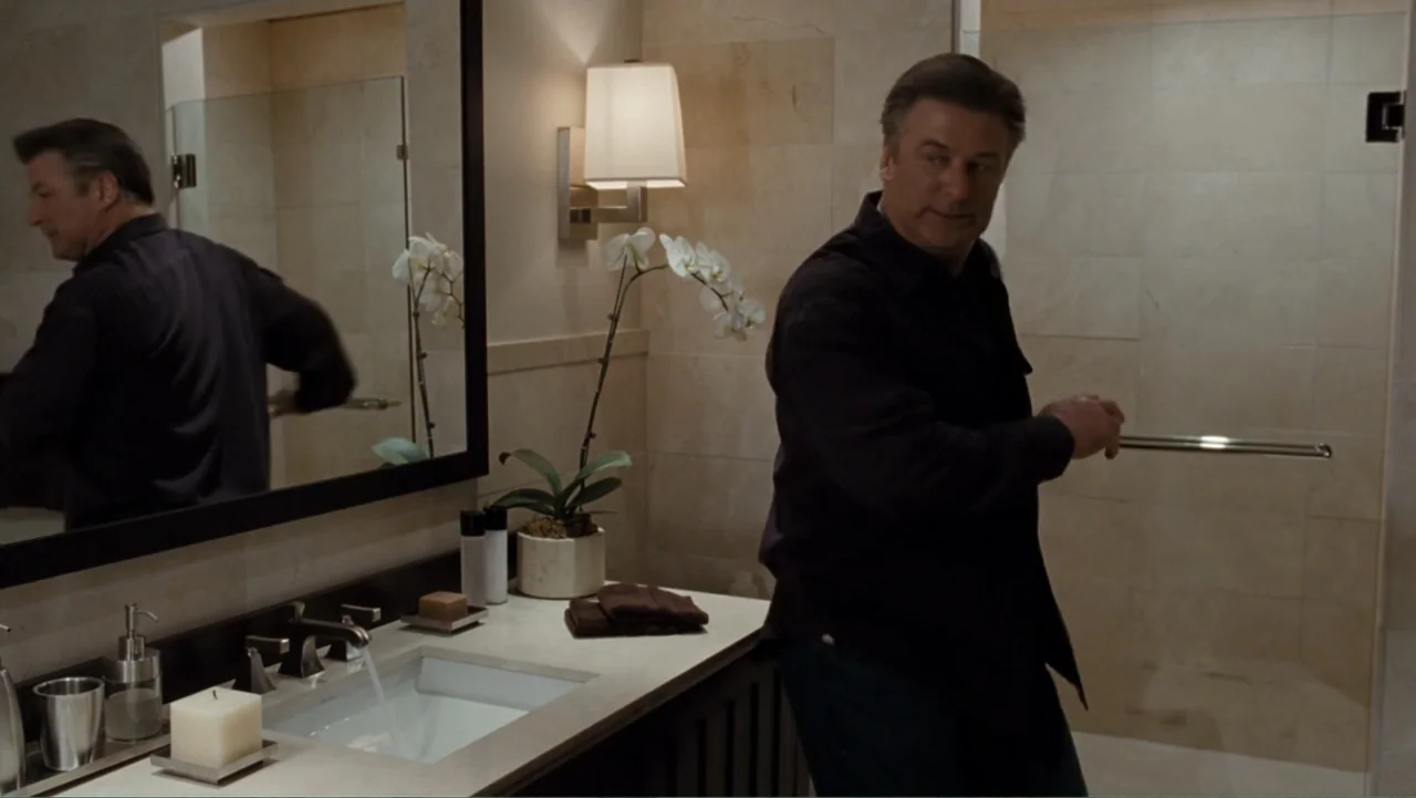 It's Complicated (2009) movie still: medium — A modern bathroom features light-colored marble tiling and a granite-topped vanity area. A man…