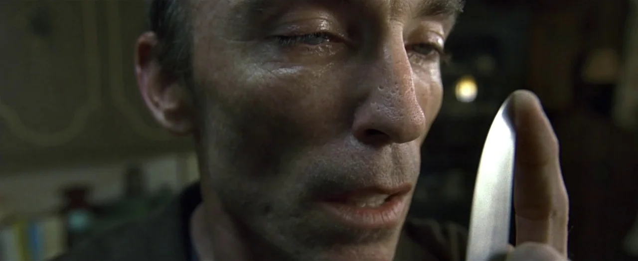 Little Children (2006) movie still: closeup — A dark indoor setting provides a dim, low-contrast backdrop for the central figure. A thin,…