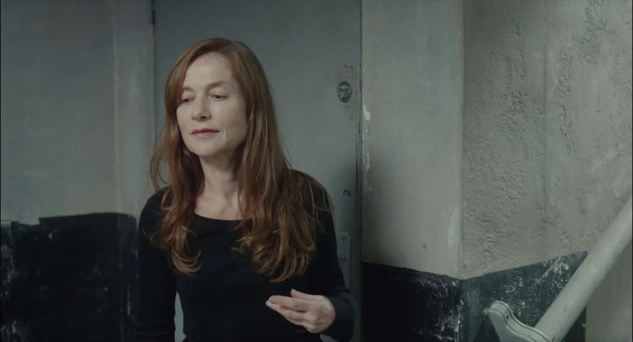 Abuse of Weakness (2013) movie still: medium — A plain stairwell features a gray metal door set into a textured concrete wall. A middle-aged woman…