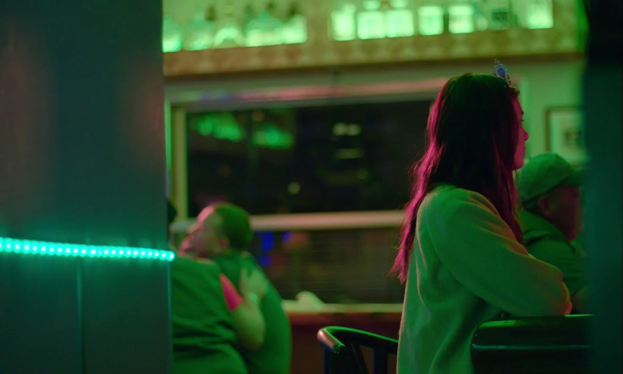 Mickey and the Bear (2019) movie still: medium — A dimly lit bar interior features green neon lighting accents behind the main subject. A woman sits…