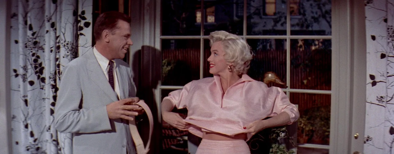 The Seven Year Itch (1955) movie still: medium — A well-lit residential room features floor-to-ceiling windows looking out onto a dark exterior…