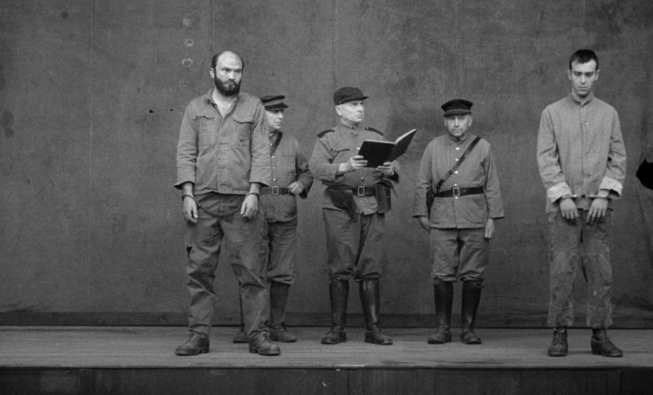 Goto, Island of Love (1969) movie still: fullbody — A bare wooden stage with a plain grey backdrop creates a sterile, minimal environment. Two…