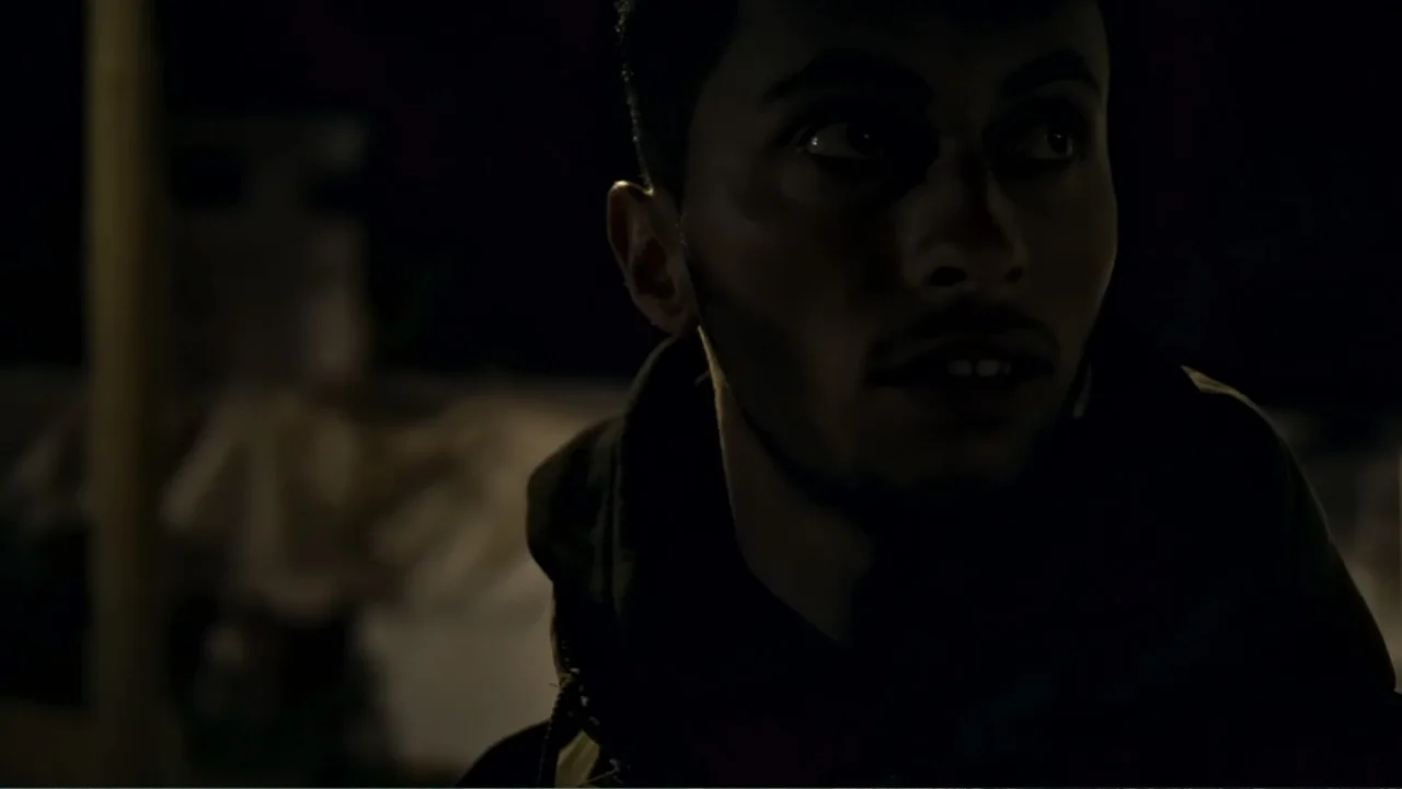 No Other Land (2024) movie still: closeup — A dimly lit room with dark surroundings hides the architectural details. A young man with stubble looks…
