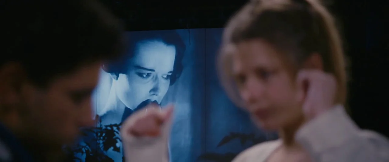 Blue Is The Warmest Colour (2013) movie still: medium — A dark space features a large projection screen displaying a black and white film. Two…