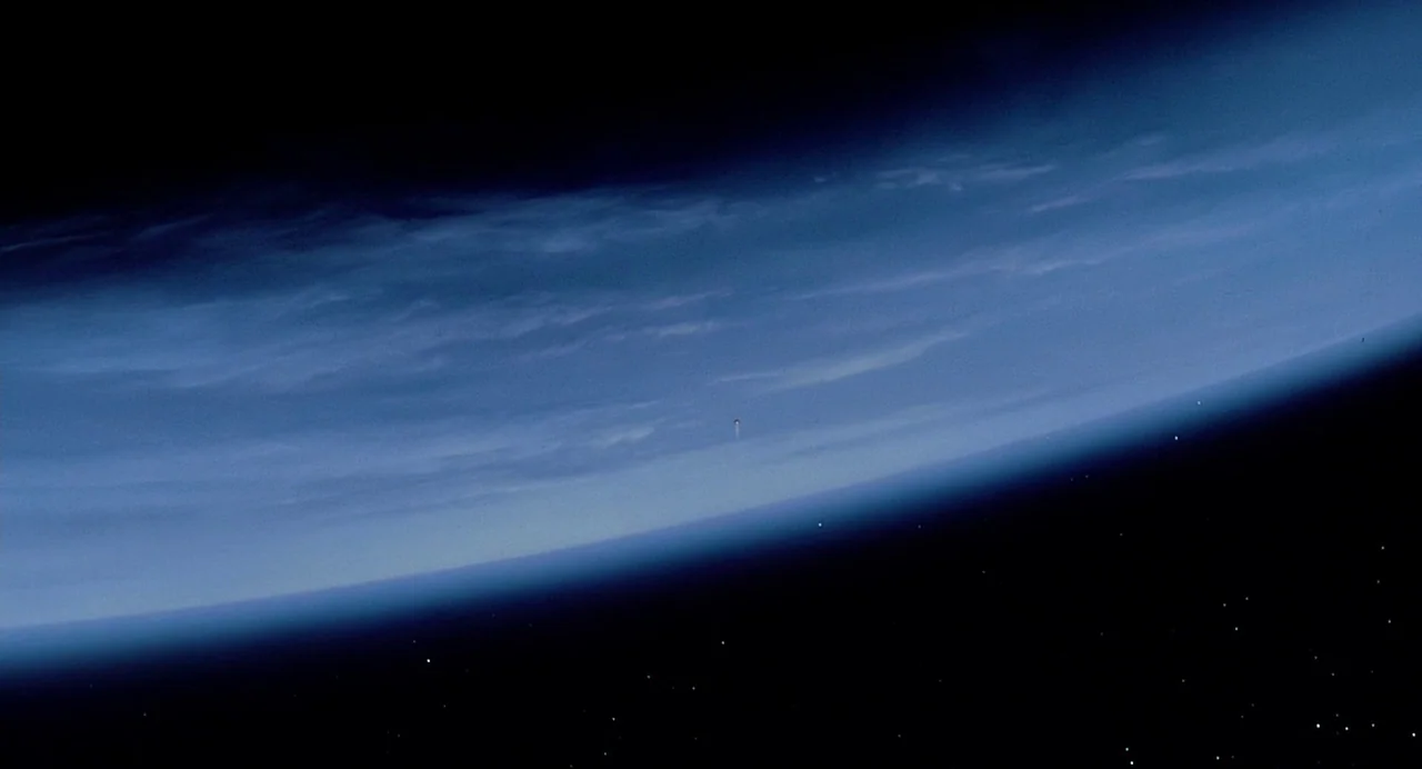 Predator (1987) movie still: establishing — The curved horizon of a planet is visible against the dark backdrop of space. A tiny spacecraft glides…