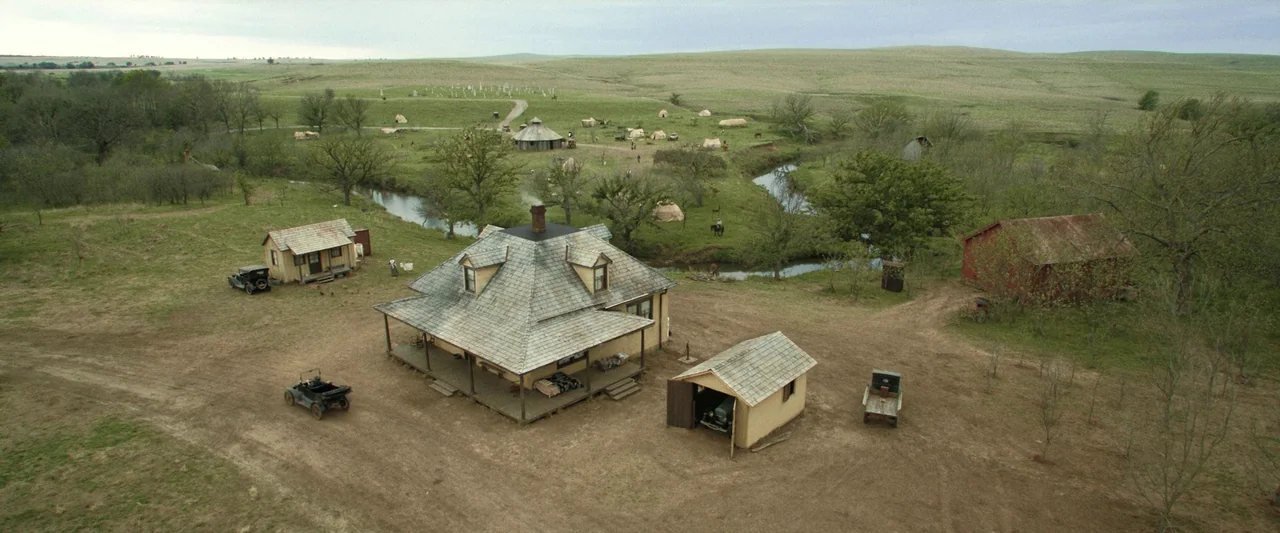 Killers of the Flower Moon (2023) movie still: establishing — A rural homestead with a central farmhouse is set amidst an expansive open green…