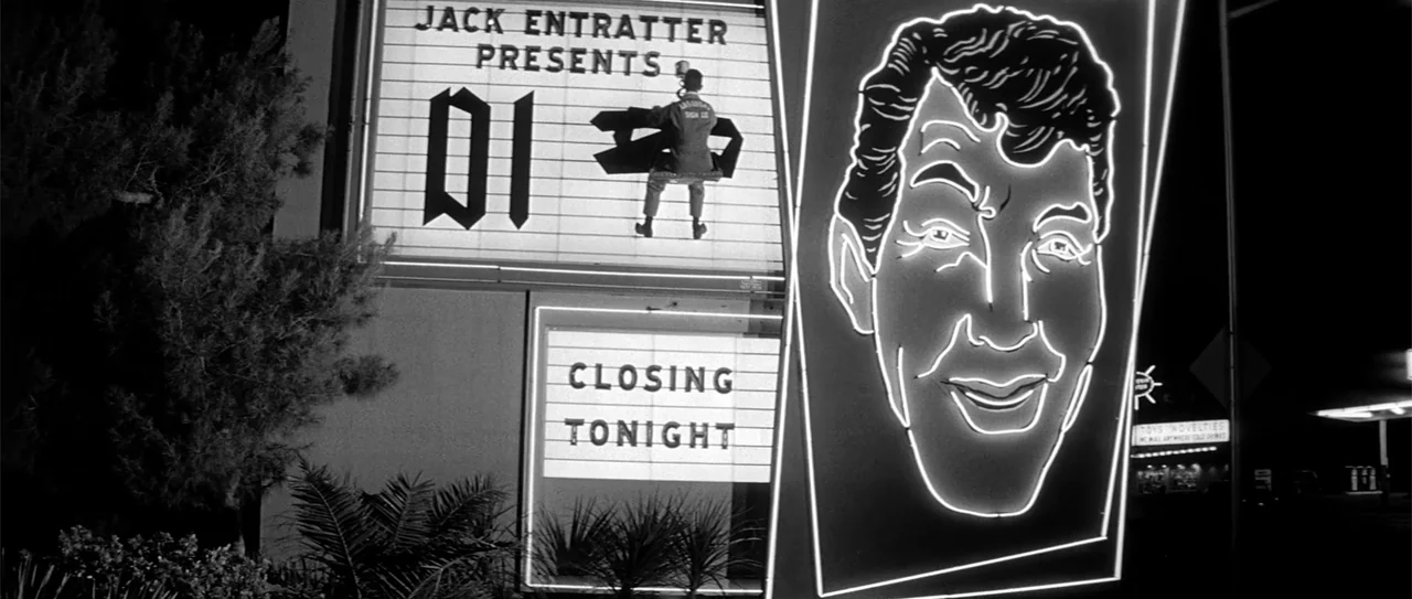 Kiss Me, Stupid (1964) movie still: wide — A night scene shows a large illuminated marquee sign displaying text and a neon face. A maintenance…