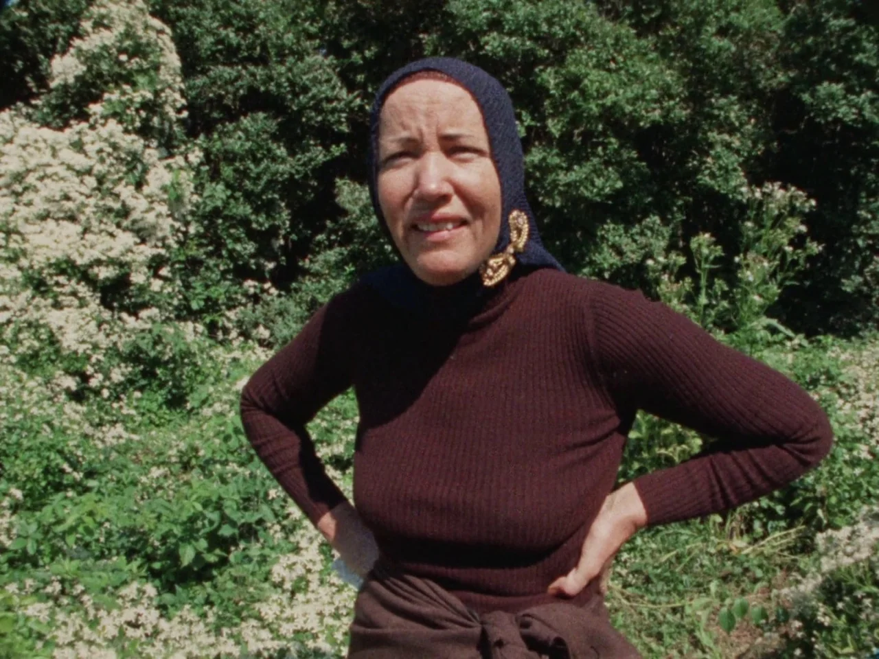 Grey Gardens (1975) movie still: medium — A woman stands in front of a dense thicket of white flowering shrubs. She is looking directly at the…