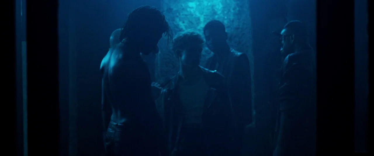 Knife+Heart (2018) movie still: medium — A dark space lit by high-contrast blue light with textured walls. Four men are positioned in a group.